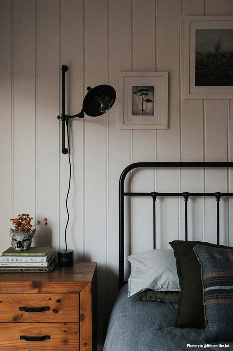 Black swing arm wall scone hanging next to a bed.
