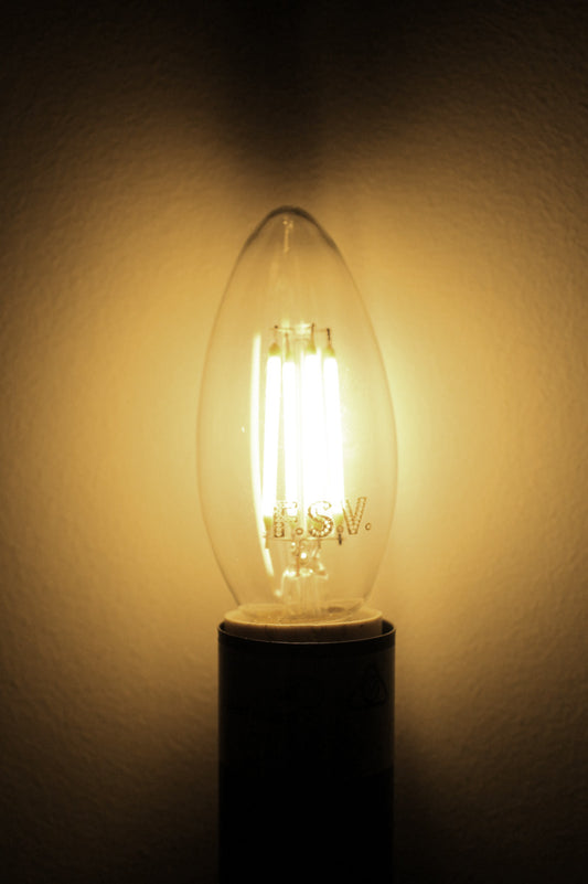 Lit E14 filament LED candle bulb giving off a warm amber glow