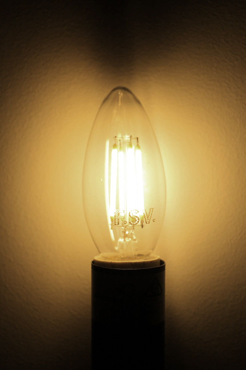 Lit E14 filament LED candle bulb giving off a warm amber glow