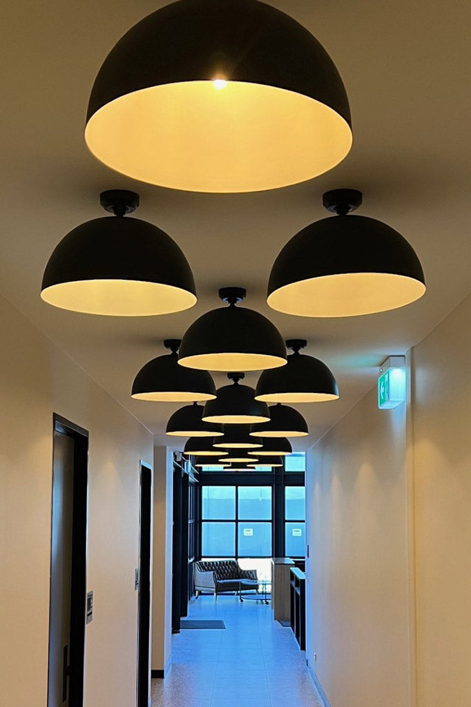 Modern black flush mount dome lights in a hallway with a view of a office room with large windows.