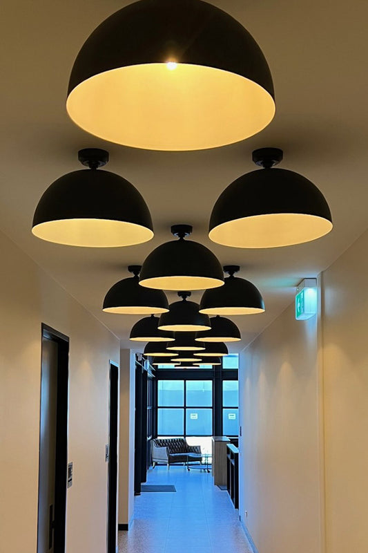 Modern black flush mount dome lights in a hallway with a view of a office room with large windows.