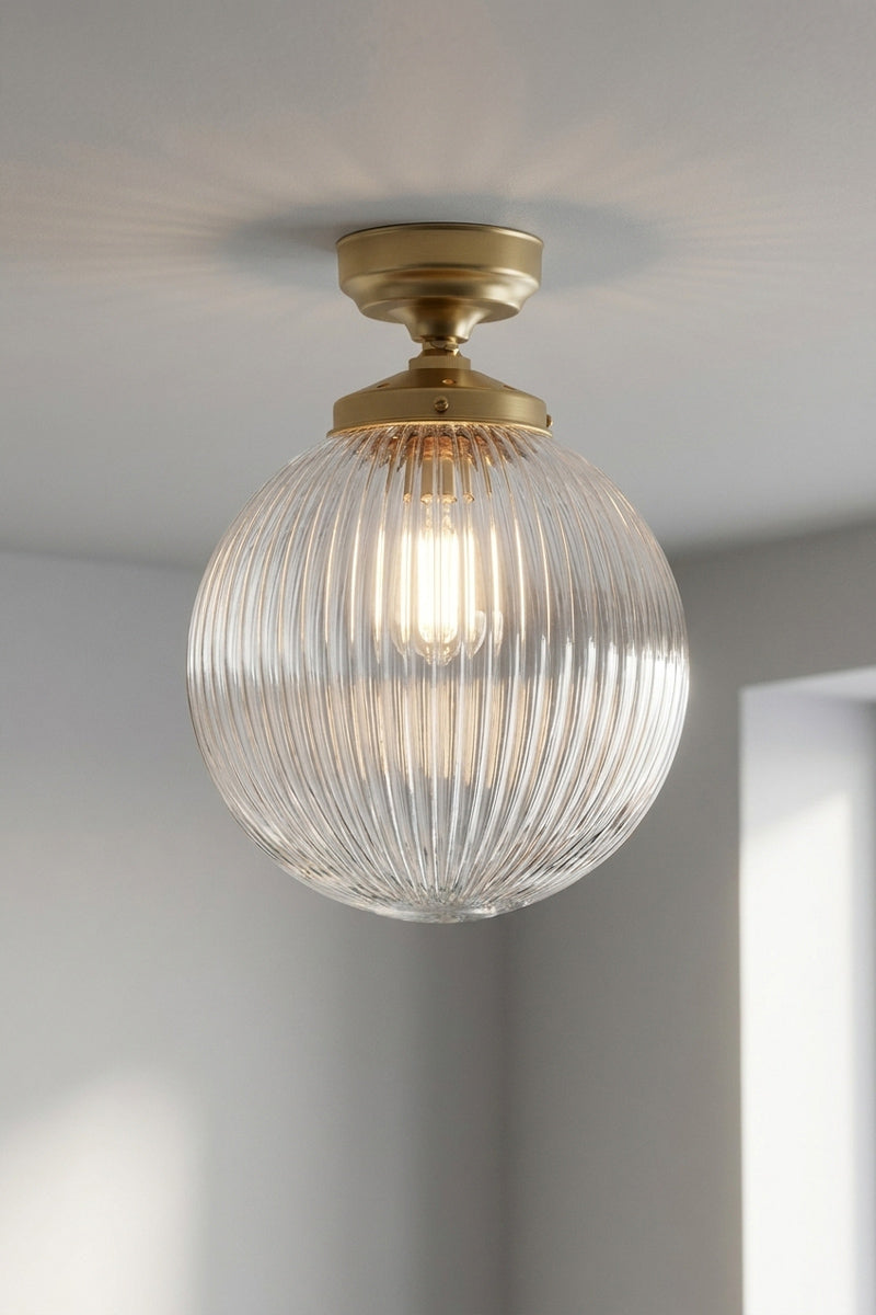 Medium clear reeded glass shade paired with a gold/brass batten holder on a white, shiplap wall. 