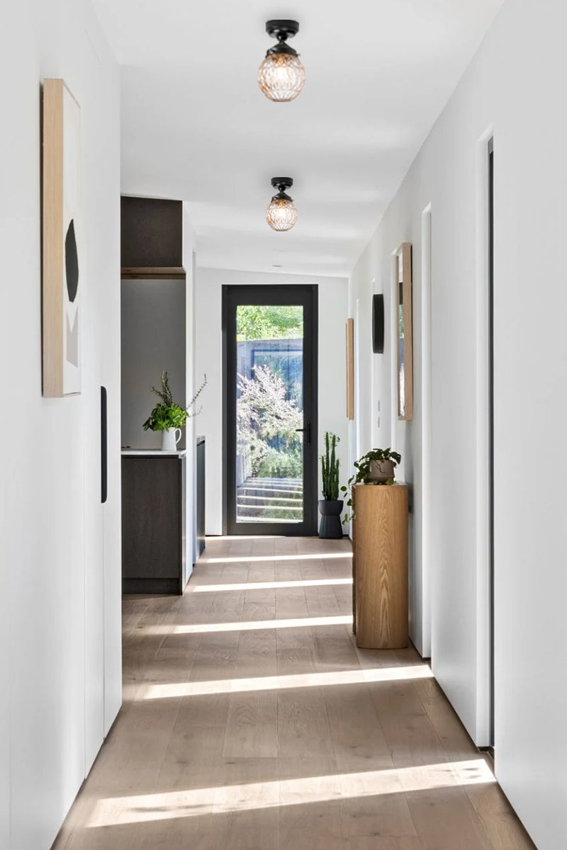 Two clear glass ball shades on black close to ceiling lights in a light filled hallway. 