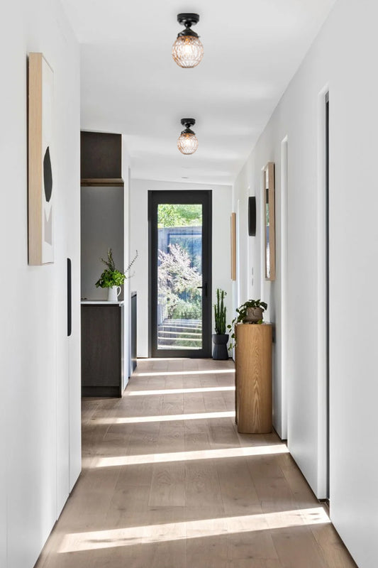 Two clear glass ball shades on black close to ceiling lights in a light filled hallway. 