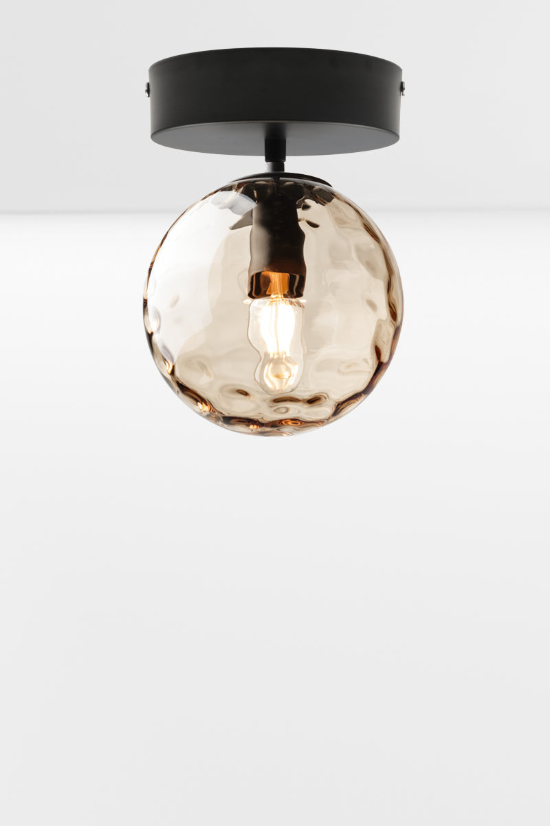 Orb glass shade in amber with a dimpled detailing on a matt black flush mount fixture. 