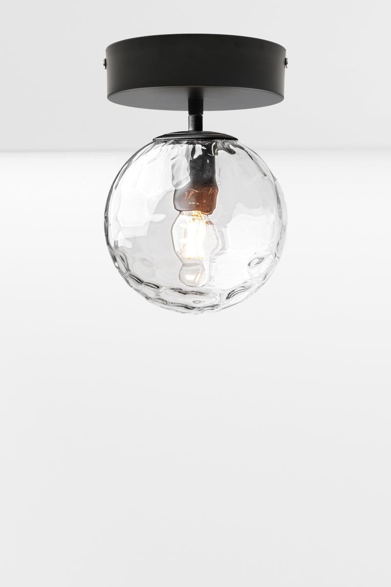 Orb glass shade in clear with a dimpled detailing on a matt black flush mount fixture. 
