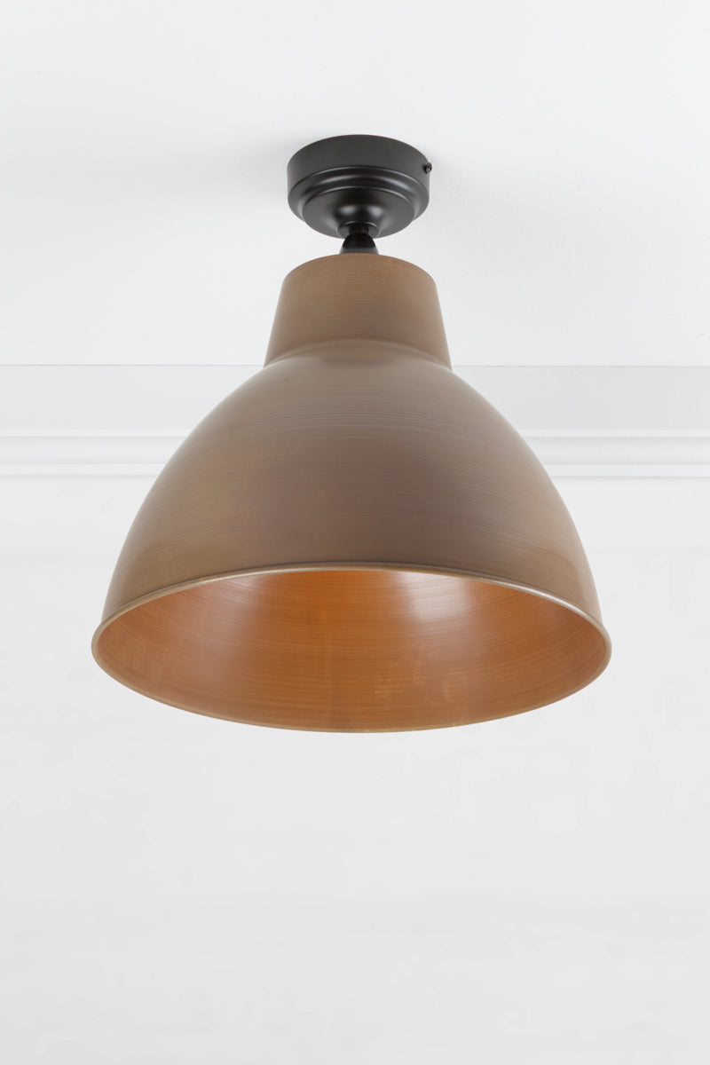 Black outdoor flush mount light with a large solid brass shade with an aged finish. 