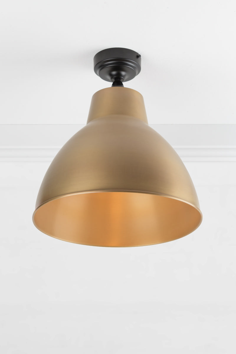 Black outdoor flush mount light with a large solid bright brass shade.
