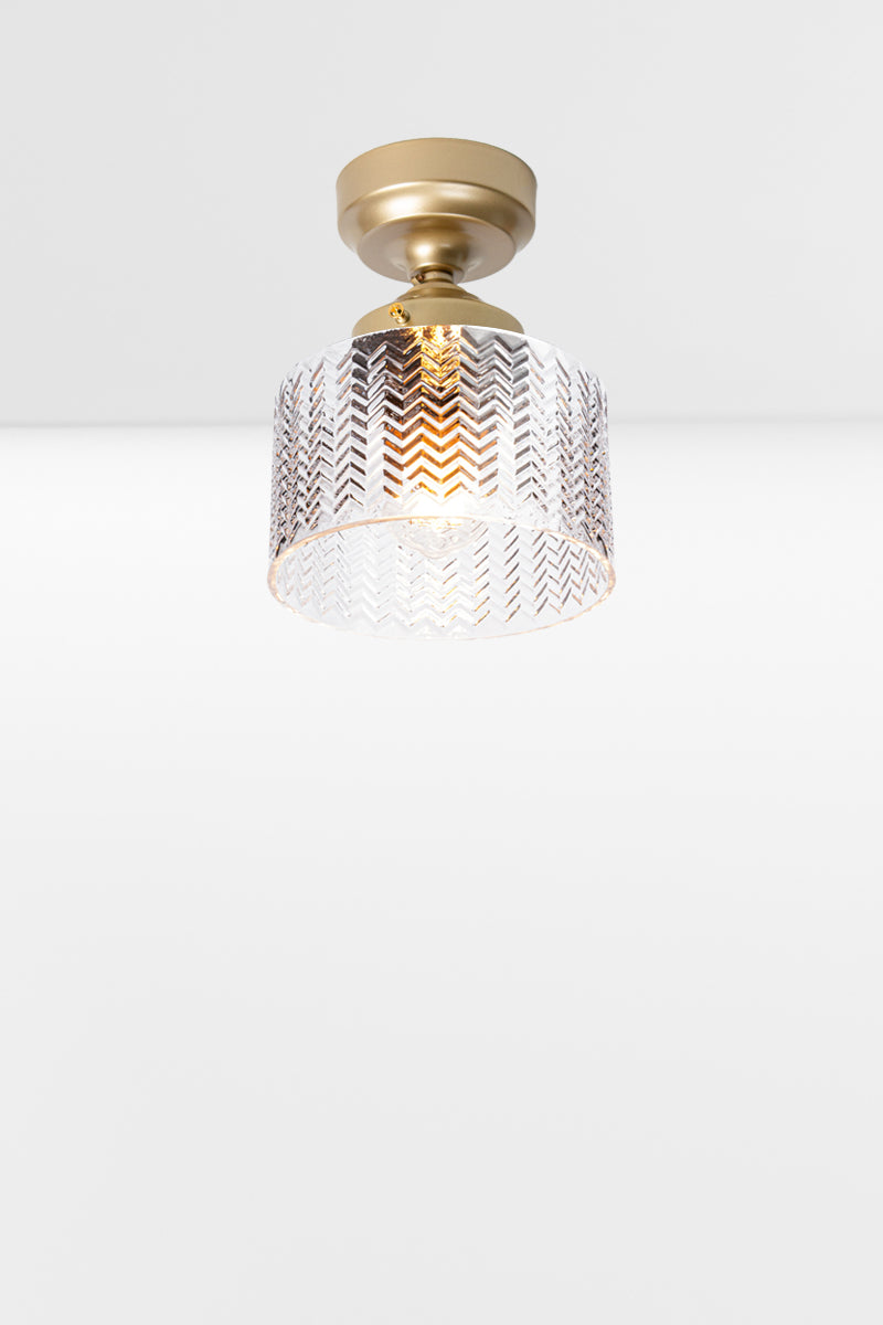 Cylindrical clear glass shade with a flat top and chevron detailing, paired with a gold/brass batten holder and gallery. 