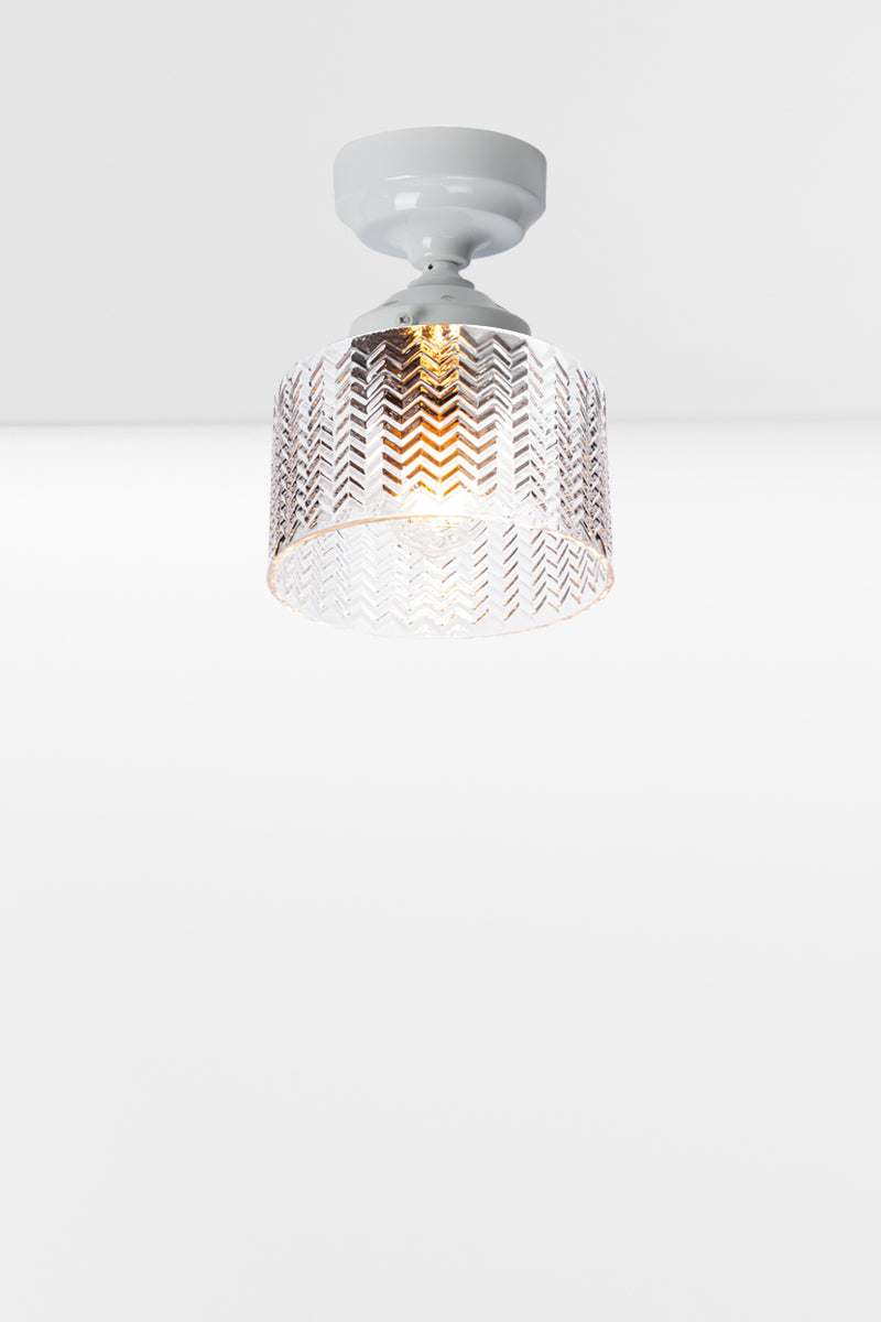 Cylindrical clear glass shade with a flat top and chevron detailing, paired with a white batten holder and gallery. 