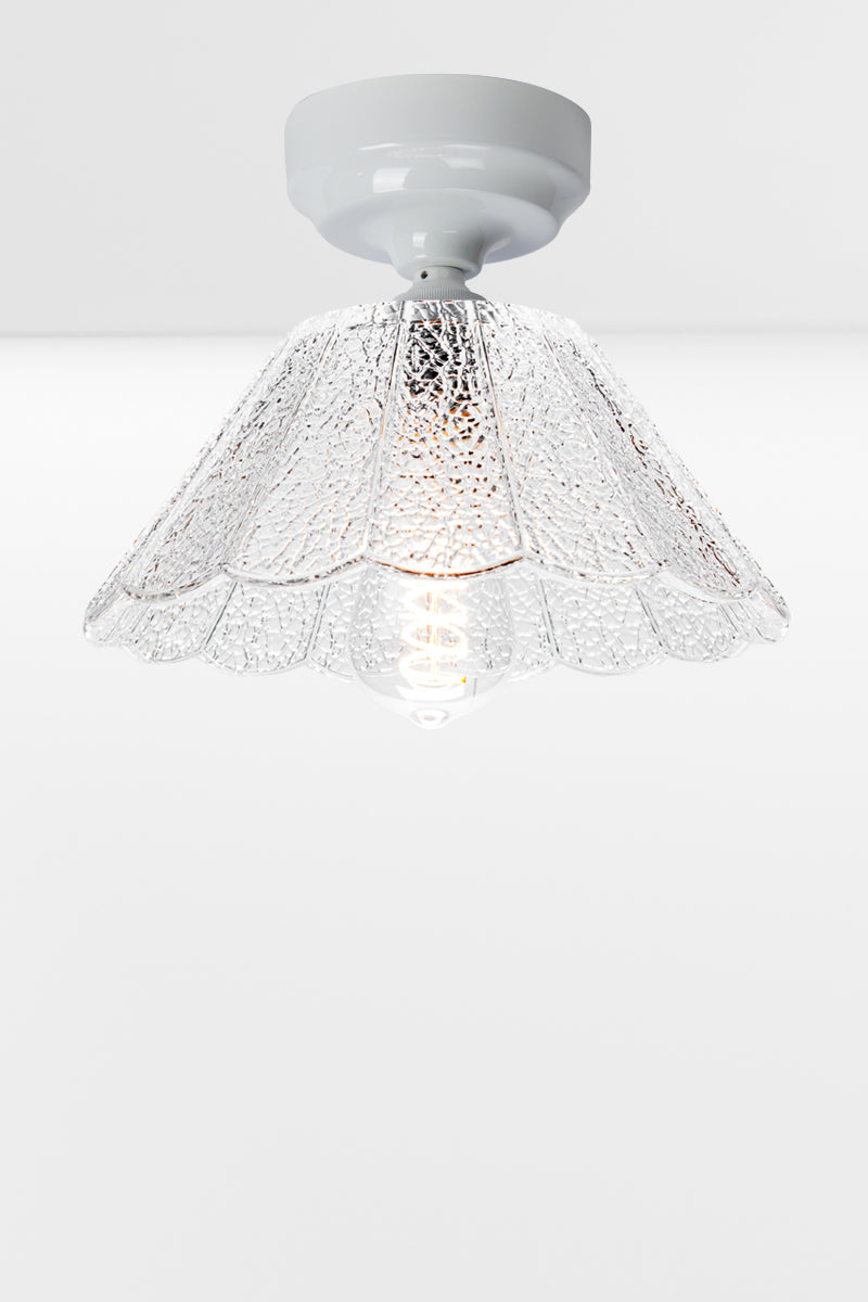  White curved batten holder holding a clear glass shade with scalloped edging and a crackle effect. 