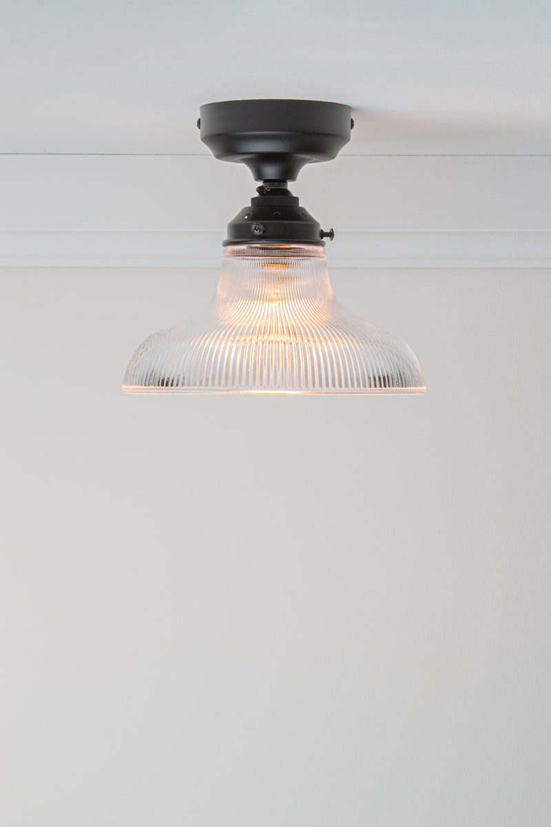Small clear holophane glass shade on a black batten holder.