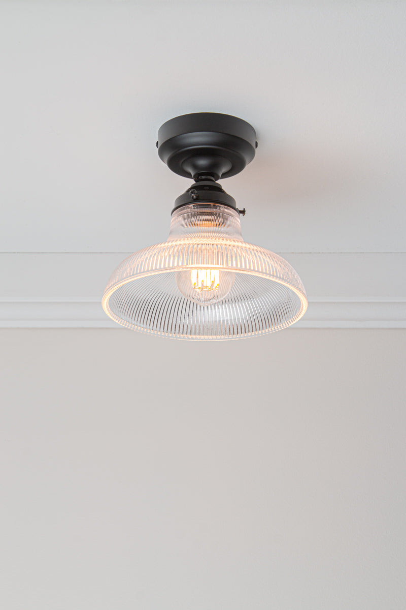 Tilted view of the Small clear holophane glass shade on a black batten holder.