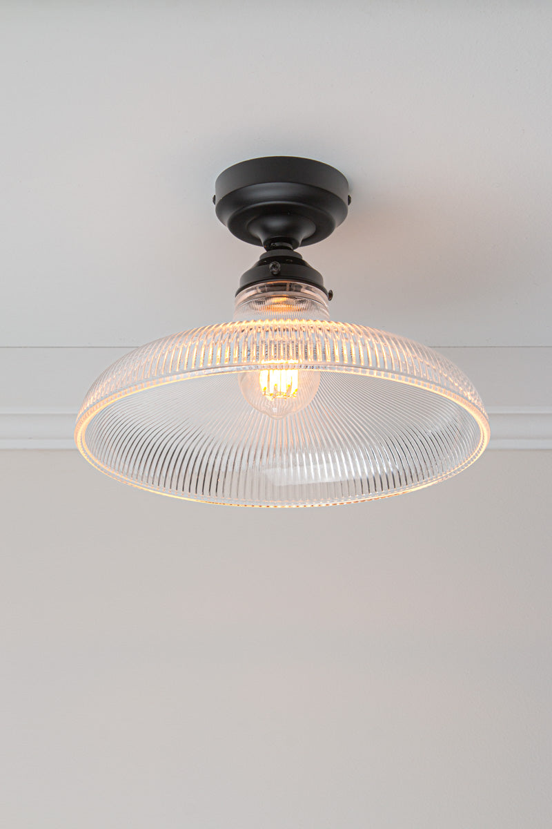 Tilted view of the large clear holophane glass shade on a black batten holder.