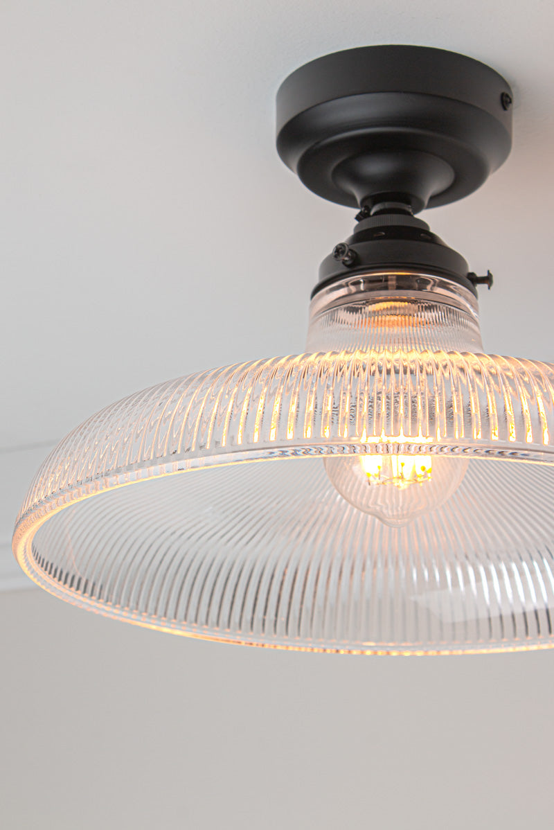 Close up of the large clear holophane glass shade on a black batten holder.