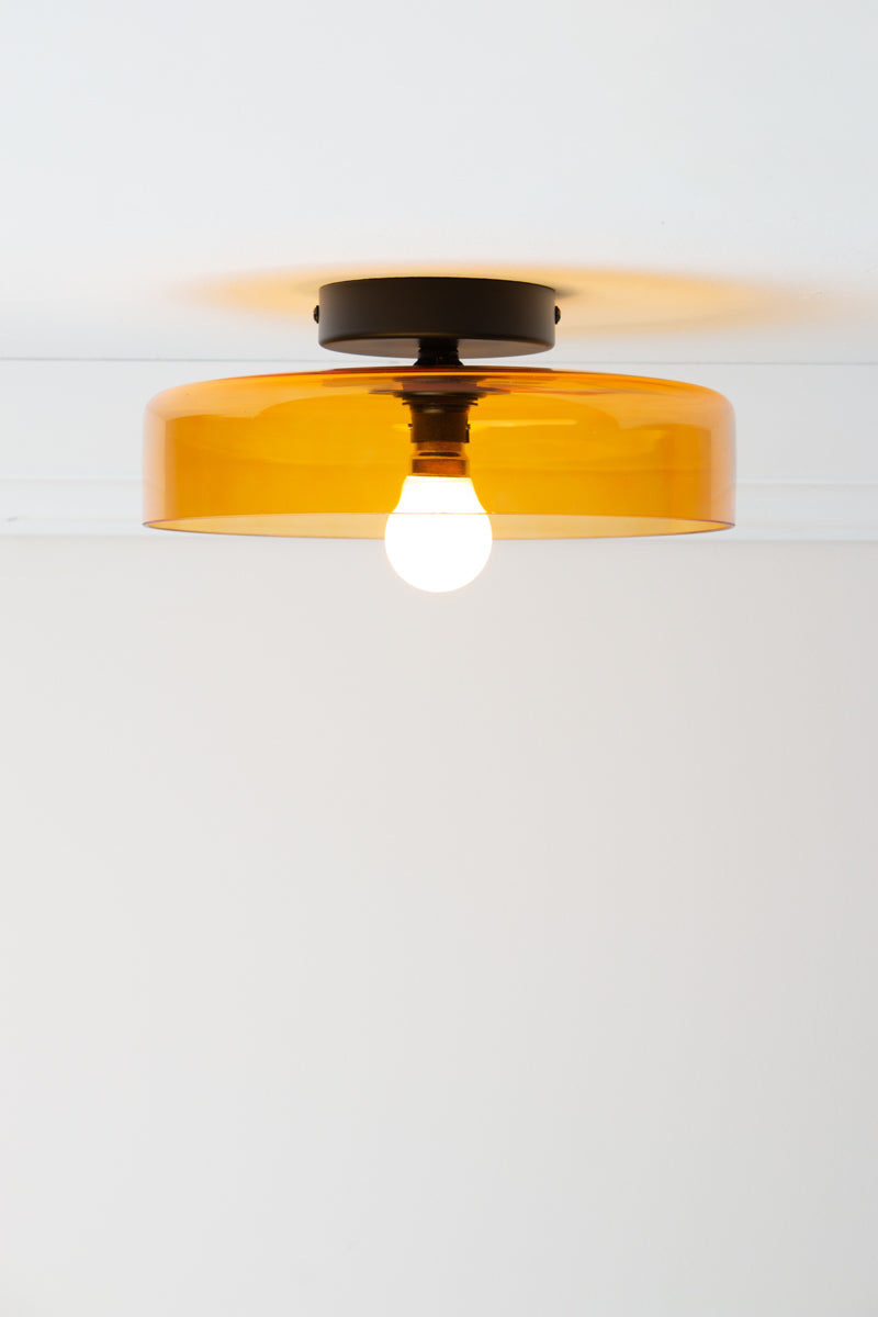 Valla Glass Ceiling Light with shallow amber glass shade and black ceiling-mounted batten holder, shown illuminated.