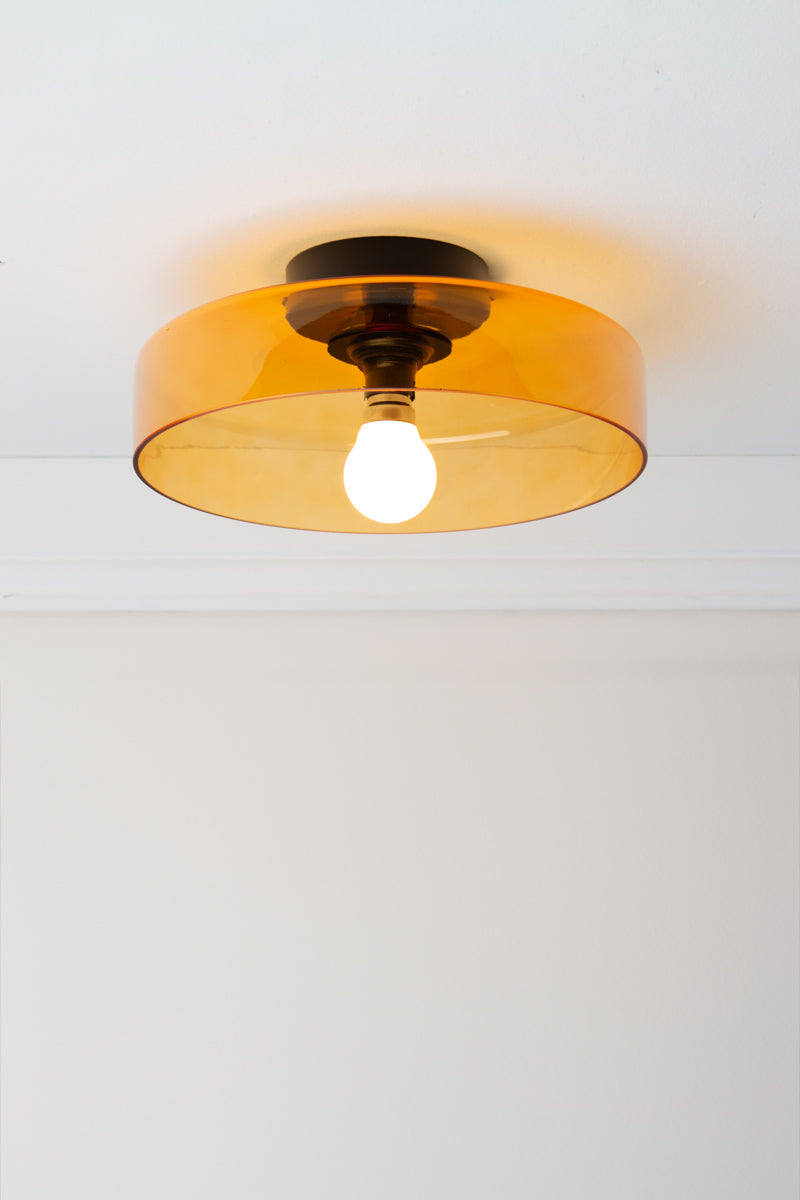 Valla Glass Ceiling Light with wide transparent amber glass shade and black ceiling fixture, illuminated against a white ceiling.