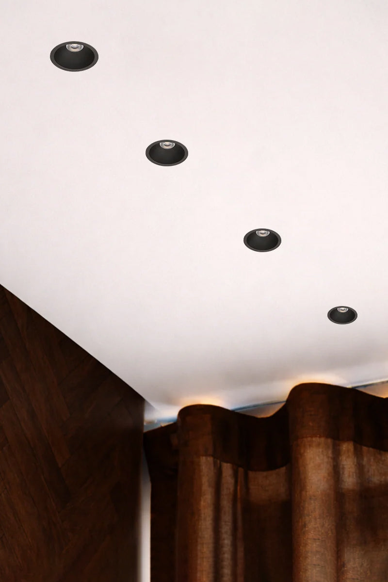 Four Black LED downlights in a white ceiling with a timber wal and curtained window. 