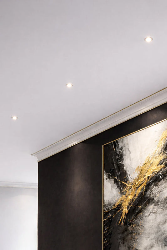 3 downlights in a white ceiling above a dark wall with modern art. 