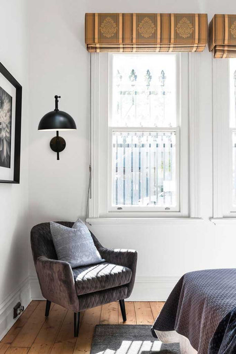 Large, black dome shade on adjustable wall arm, hanging over an armchair. 