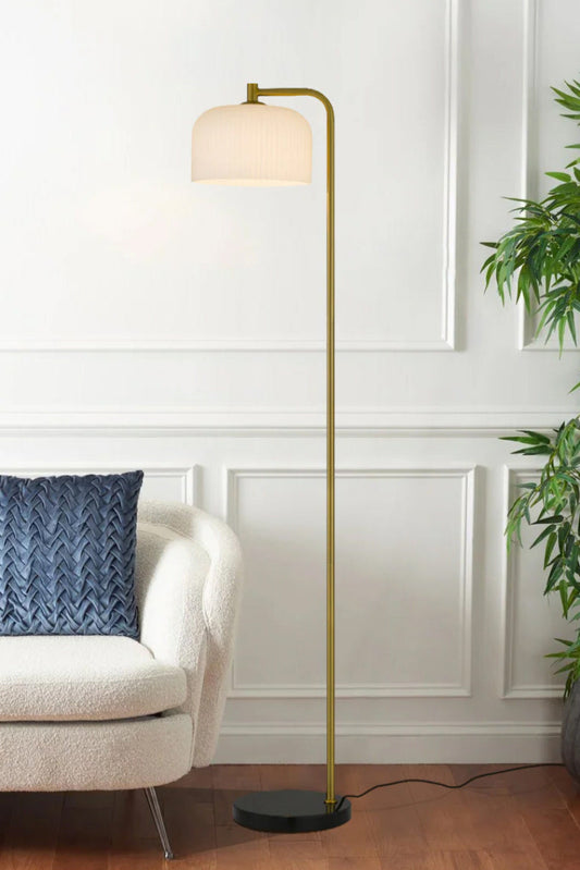 Floor lamp with a black marble base, iron body with an antique gold finish and a glass she with an opal ribbed finish in a bright living space.