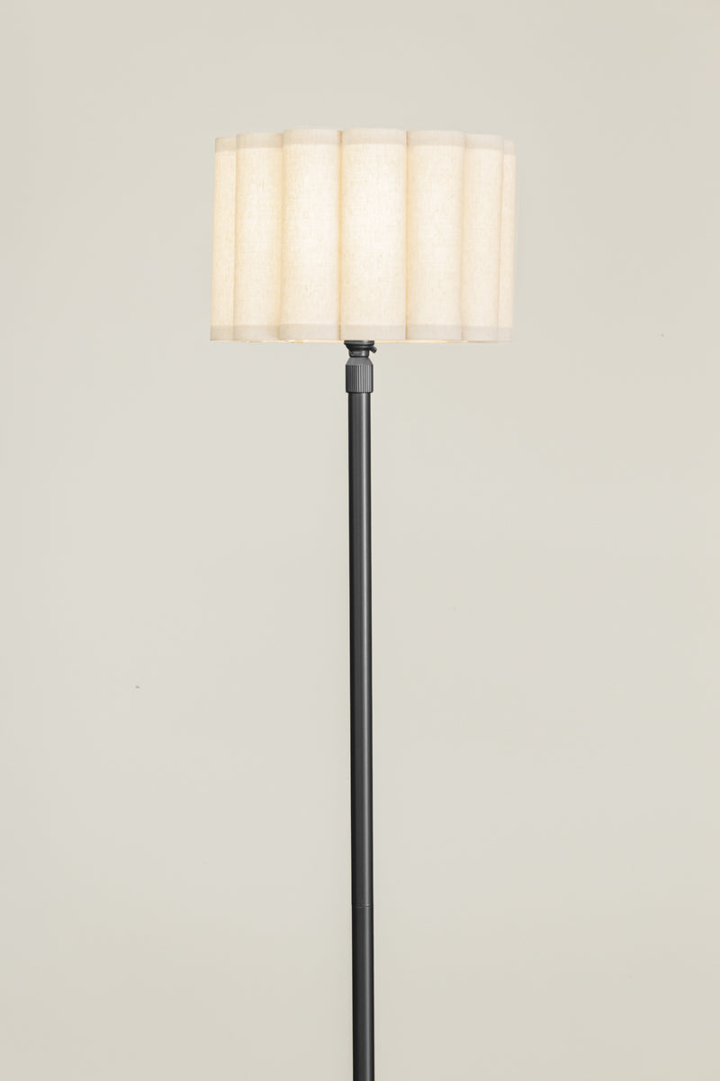 Black candle stick floor lamp with a fabric lampshade on a timber floor and muted background. 