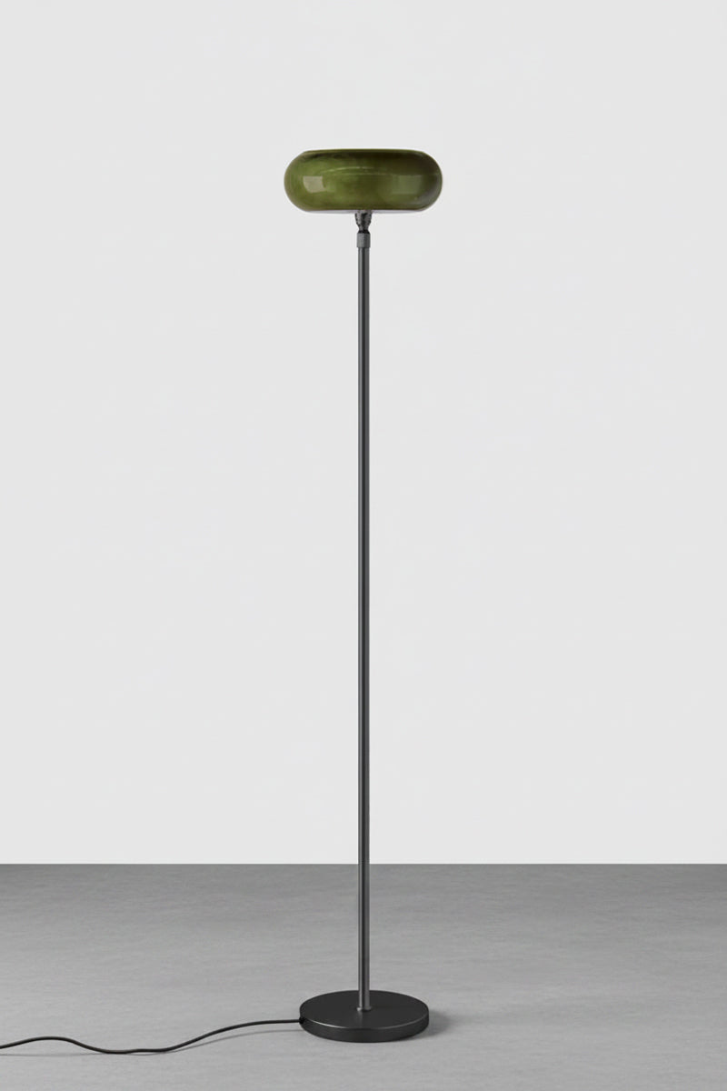 A modern floor lamp with a matte black metal stand and a rounded, forest green glass shade, set against a minimalist light gray background.