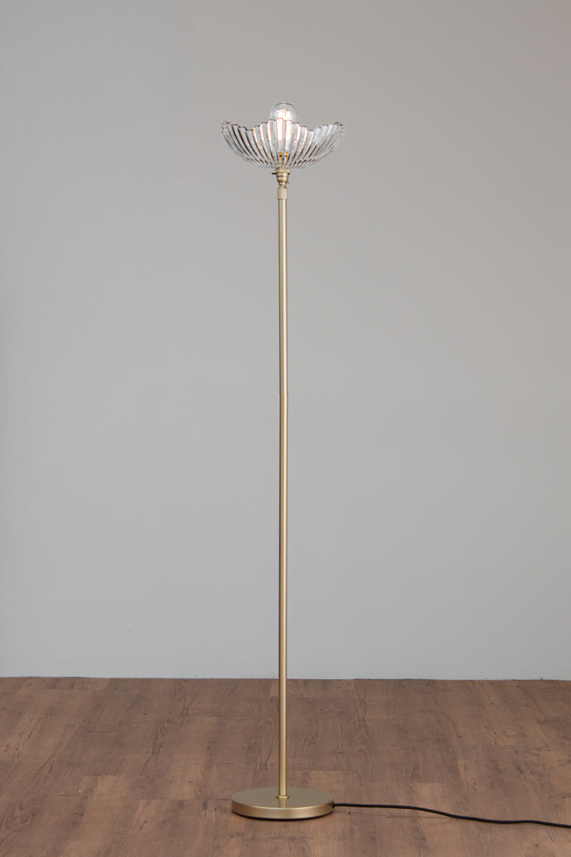 Hepburn Glass Floor Lamp with a gold/brass stand and art deco inspired clear glass shade on a timber floor. 