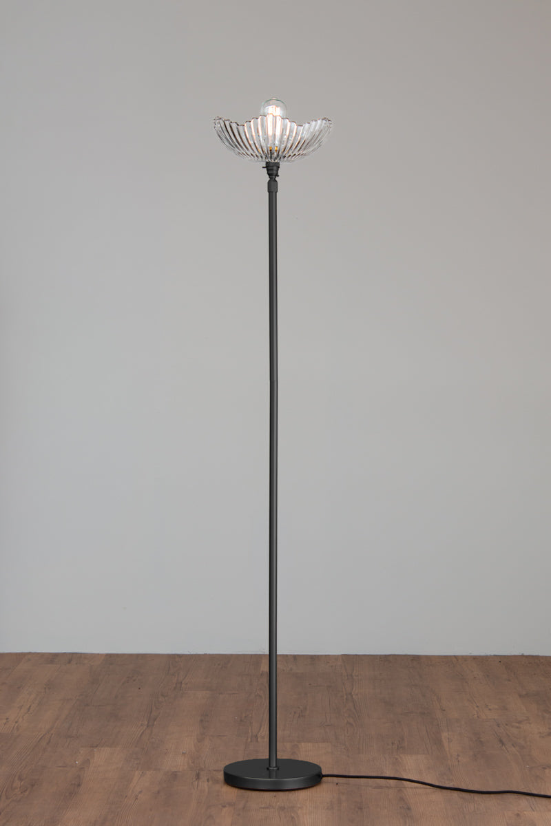 Hepburn Glass Floor Lamp with a black stand and art deco inspired clear glass shade on a timber floor. 
