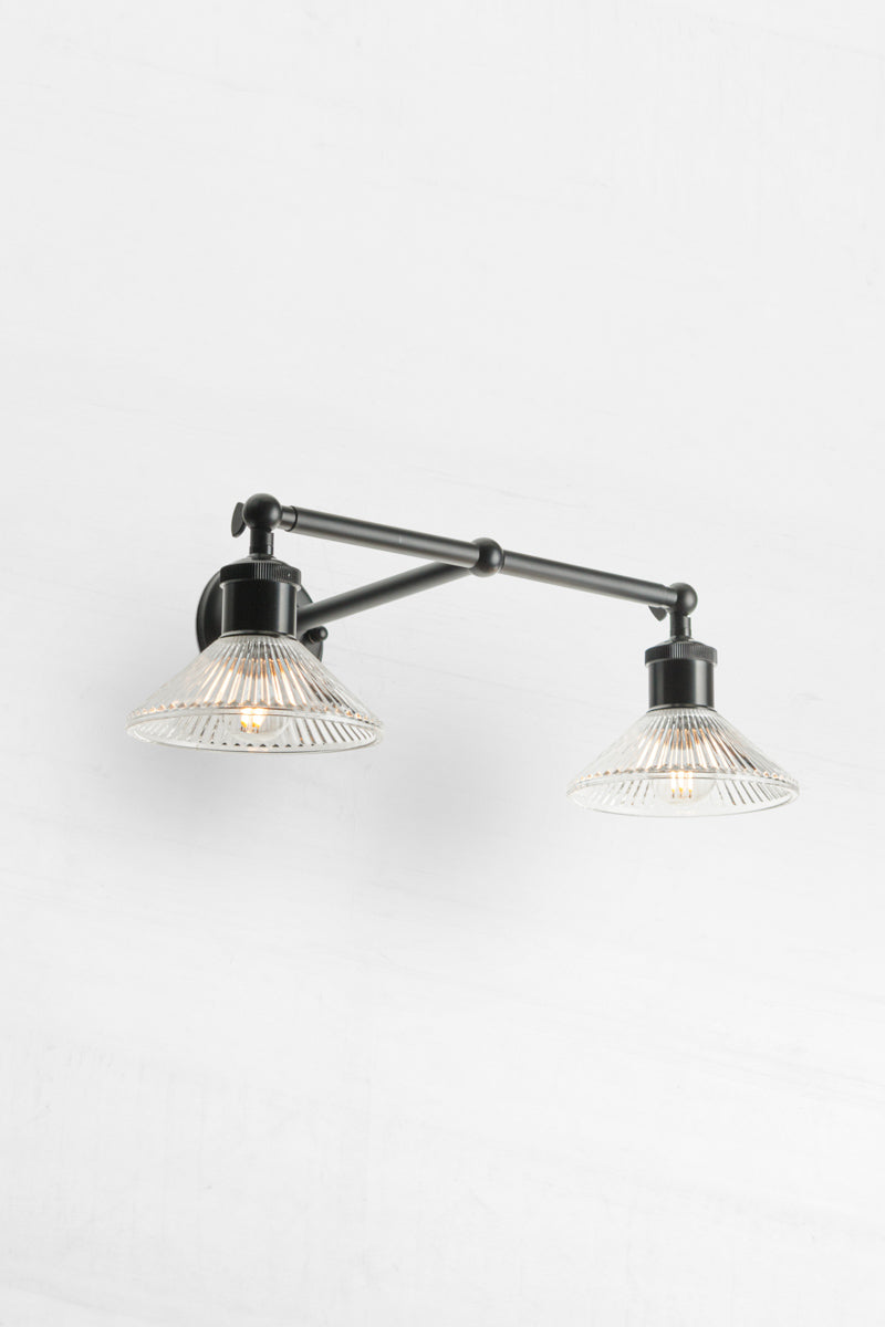 Angled view of the Black double swivel wall sconce with two clear reeded glass shades. 