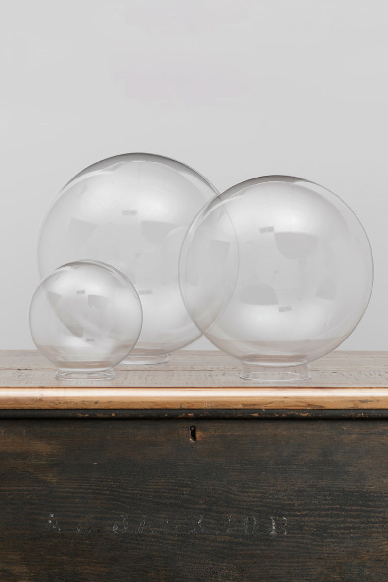 Three clear glass ball shades in a small, medium and large size on a timber bench 