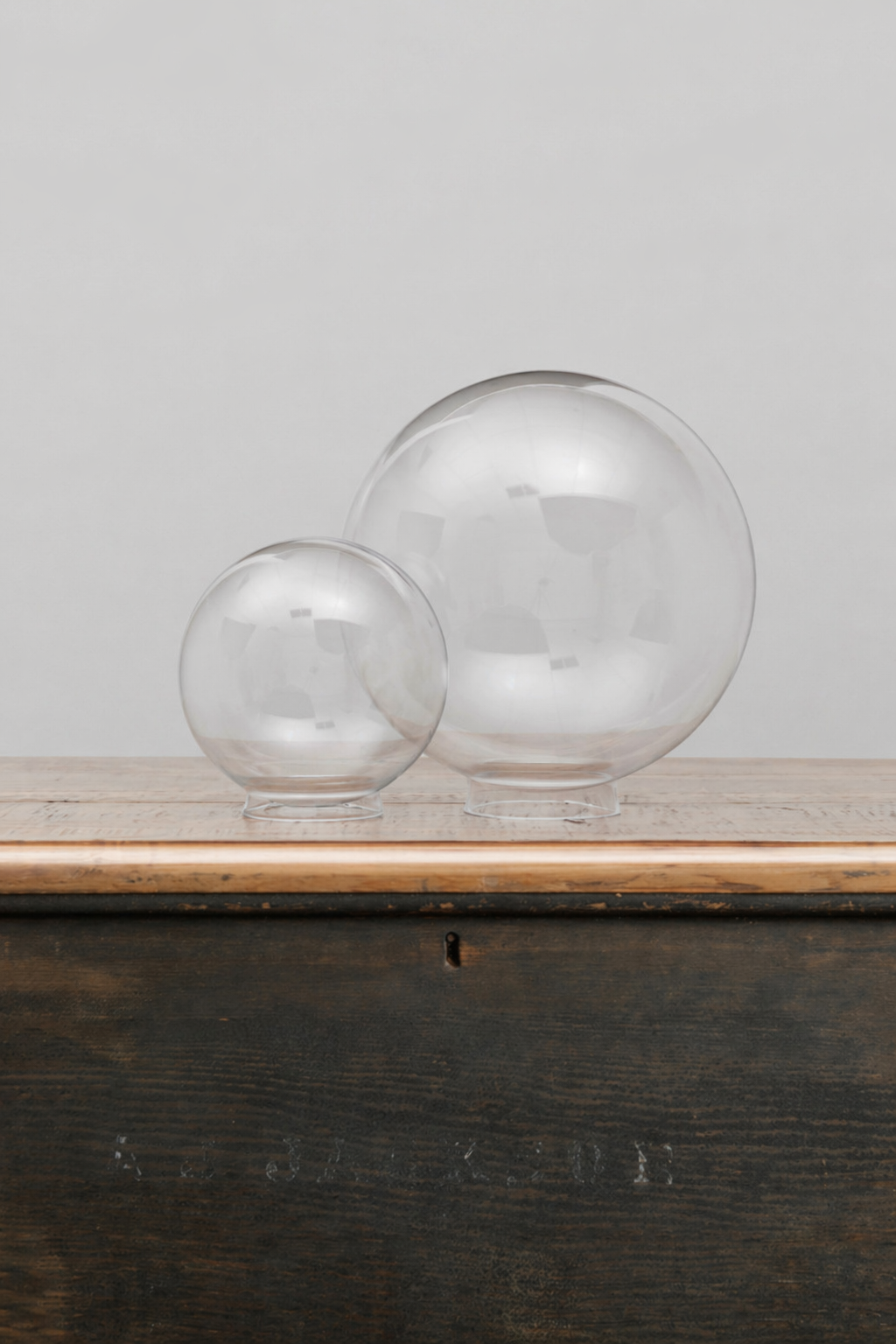 Small and medium clear glass ball shades on a timber bench. 