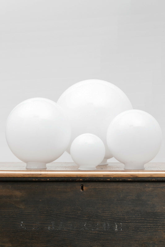 Opal glass ball shades in four sizes placed on a timber bench against a grey wall. 