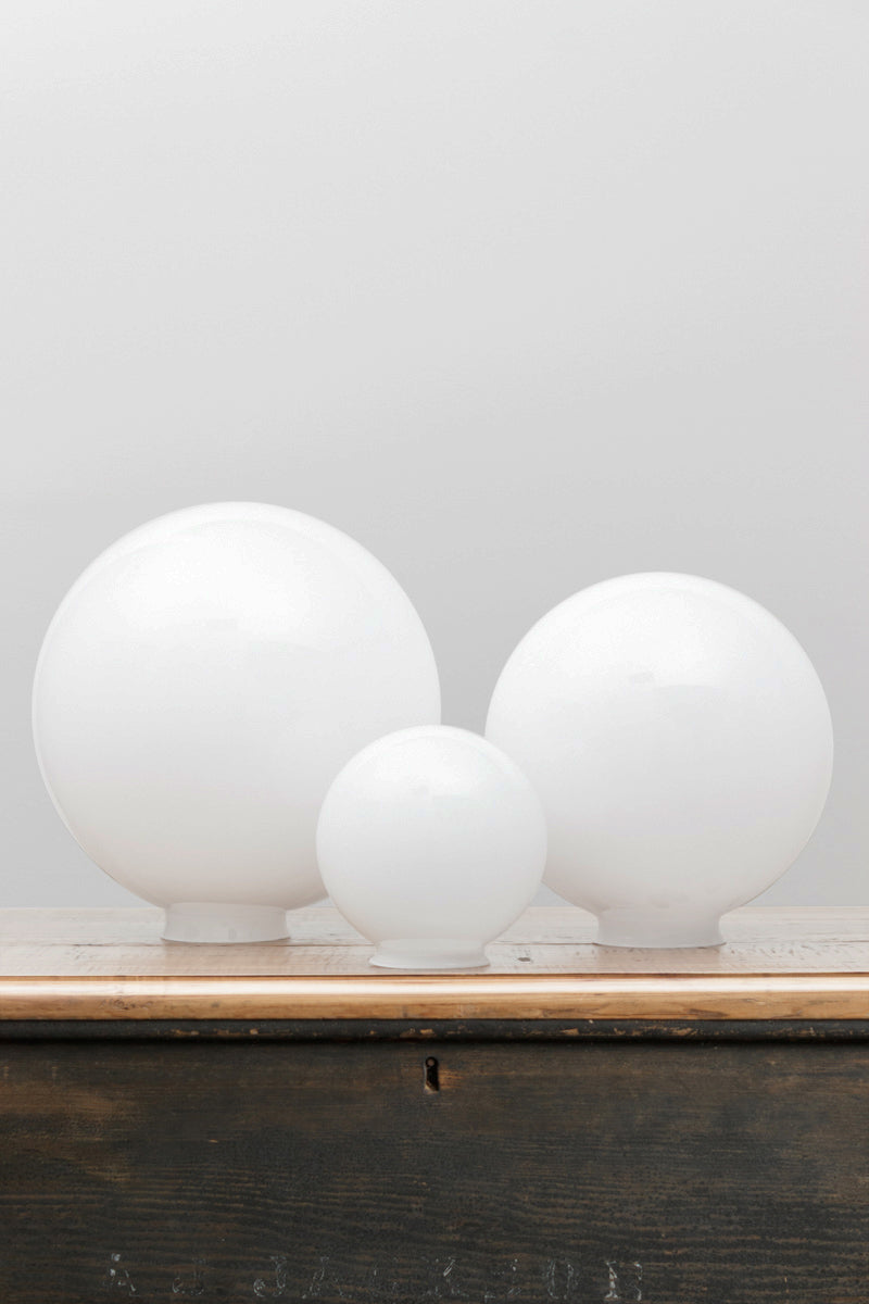 Three opal glass ball shades in a small, medium and large size on a timber bench 