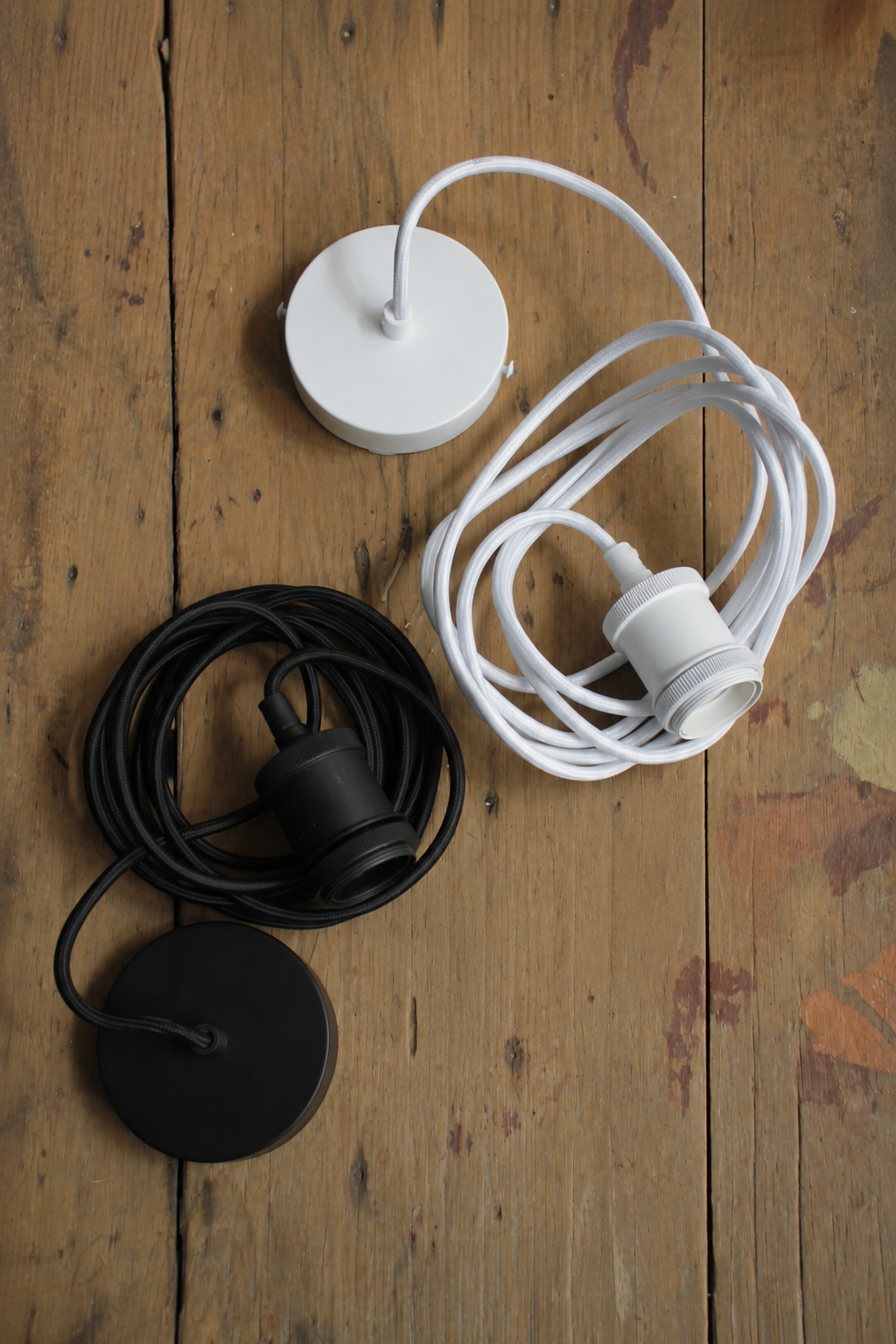 A black and a white E27 cloth cord pendant suspension on a timber surface. 