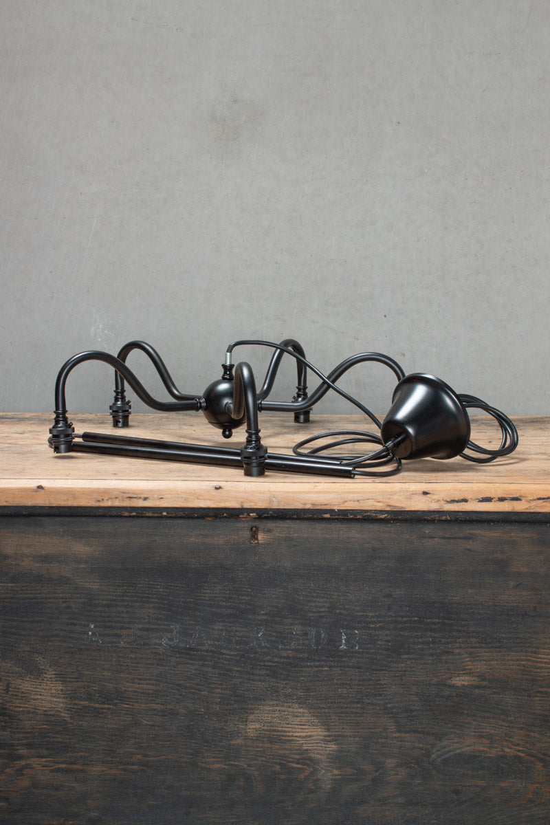 5 light black disassembled gooseneck chandelier frame on a timber bench. 