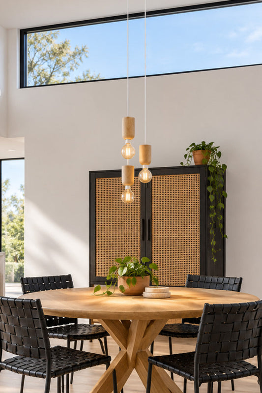 A modern dining room scene with a round natural wood table surrounded by black woven chairs, under a multi-light pendant fixture. 
