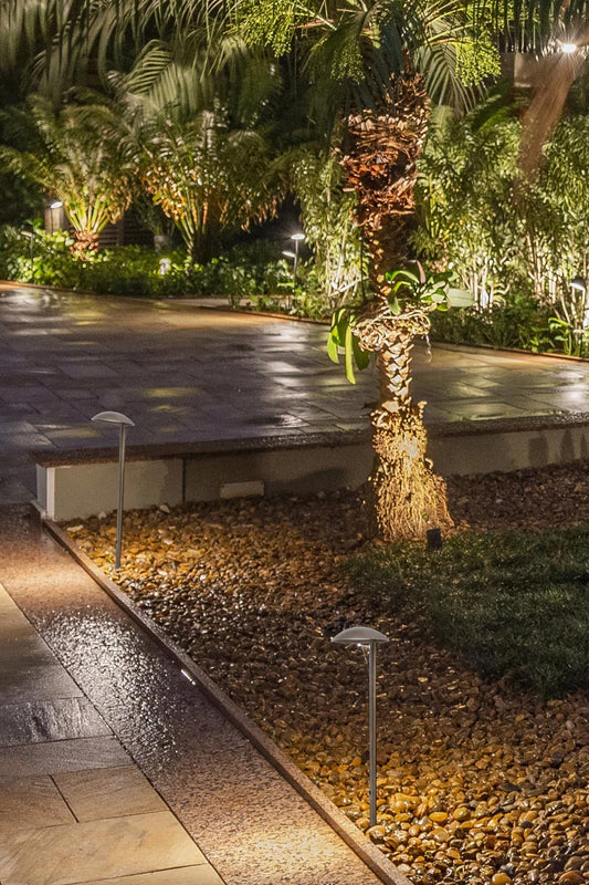 Two spike lights in black in a rock garen bed along a pathway. 