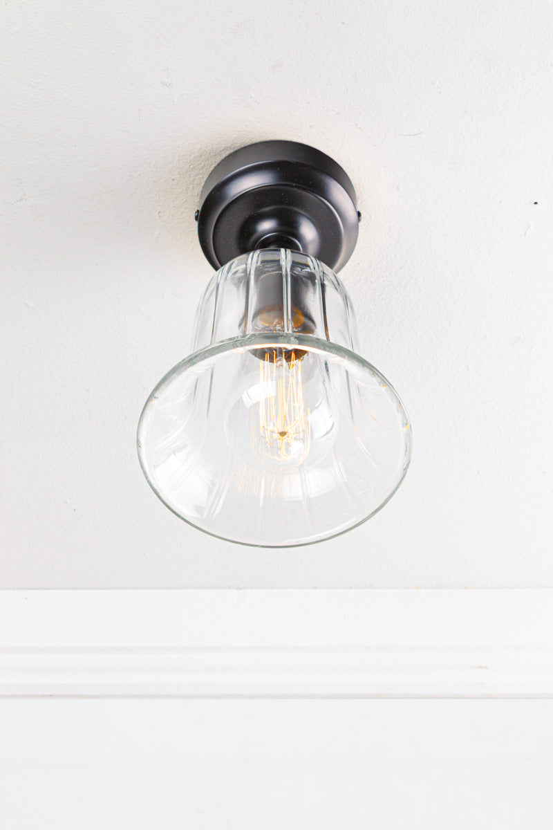 Clear glass, bell shaped shade placed on a white ceiling with a black batten holder.