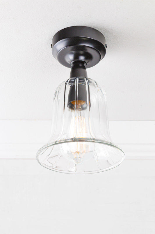 Black batten holder with a clear glass, bell shaped shade placed on a white ceiling. 