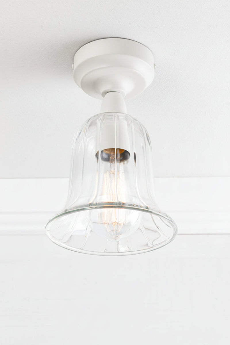 White batten holder with a clear glass, bell shaped shade placed on a white ceiling. 