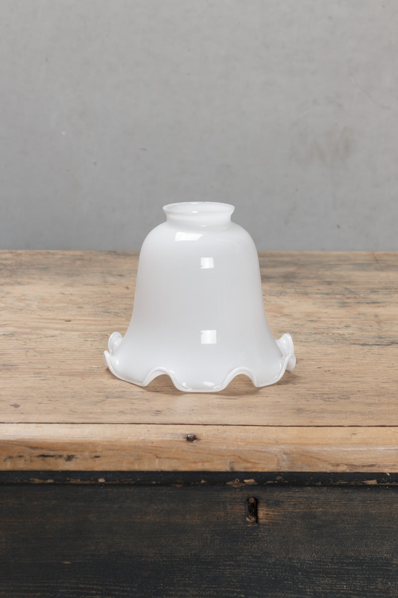 Opal glass bell shaped shade with delicate scalloped edging, placed on a timber bench. 