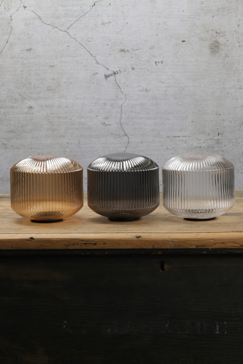 The three finish options of reeded glass shades on a timber bench with a concrete background. 
