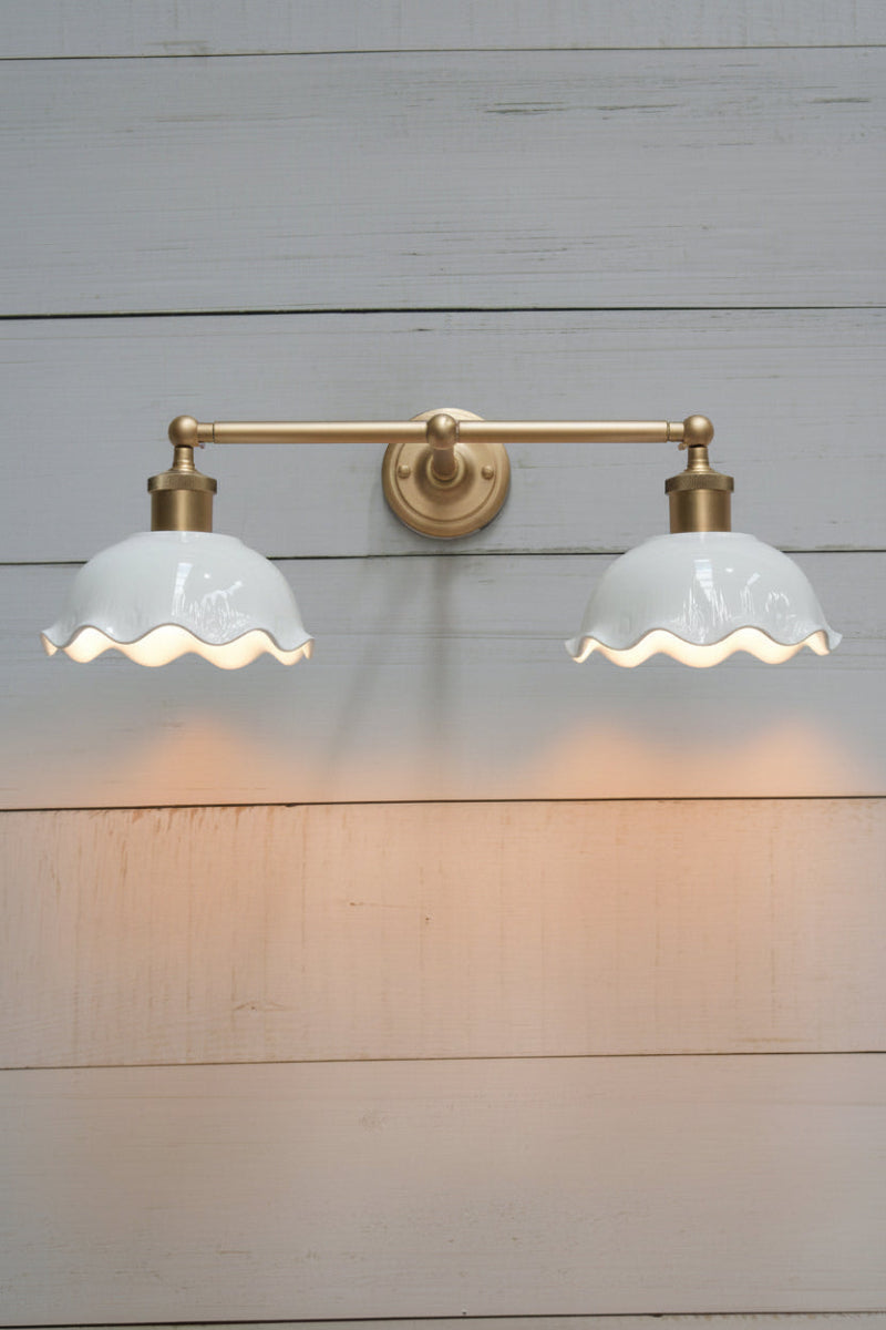 Gold/brass double swivel wall sconce with two white gloss ceramic shades with a frilled edge detail. 