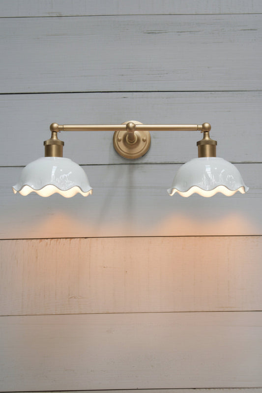 Gold/brass double swivel wall sconce with two white gloss ceramic shades with a frilled edge detail. 
