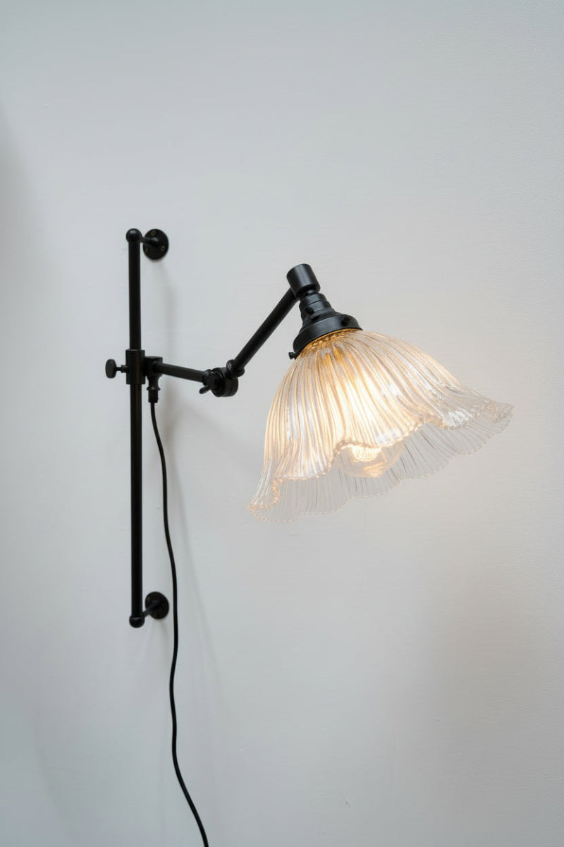 Black swing arm wall fixture with a lrage clear shade featuring a frilled edge and reeded detailing
