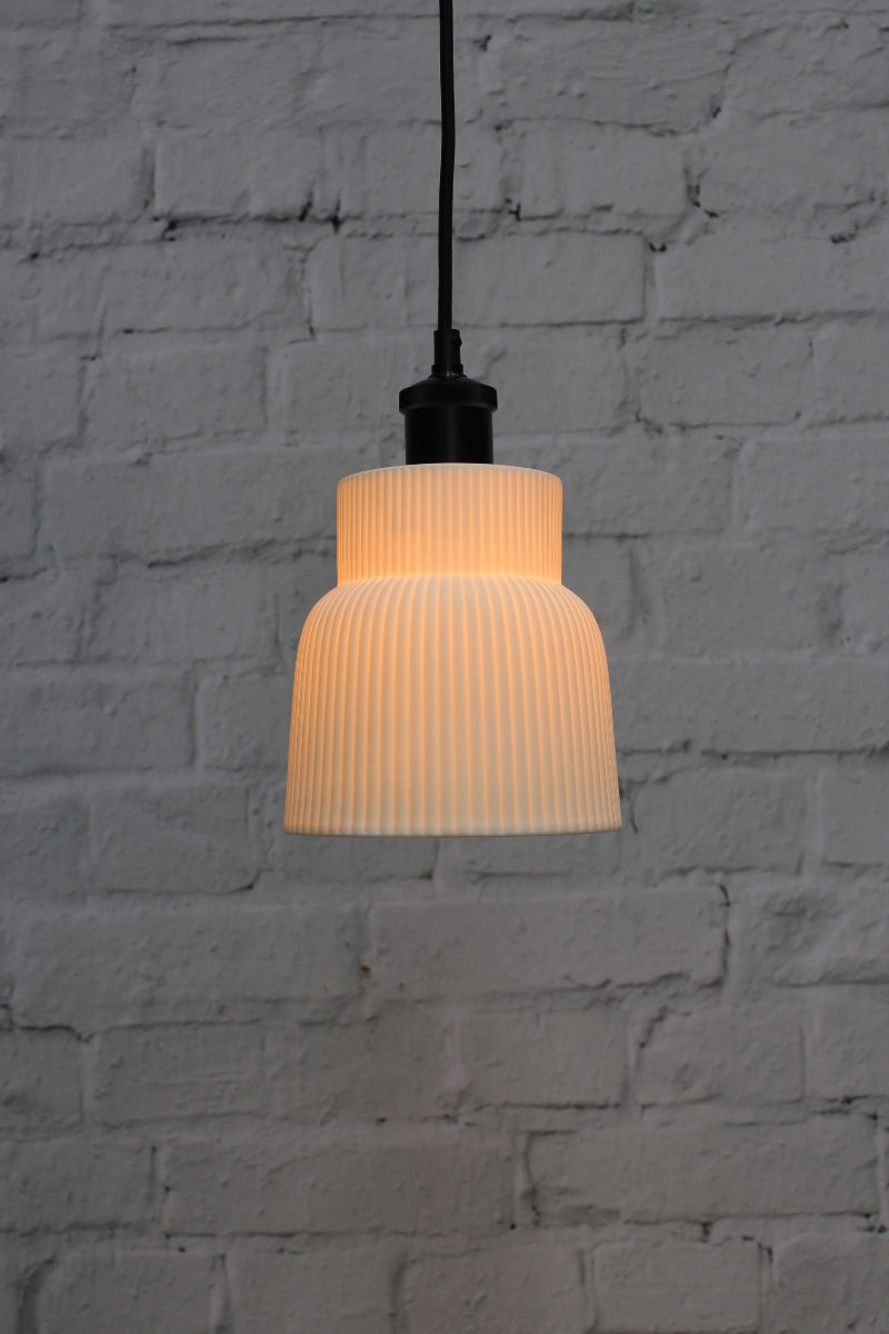 Ceramic pendant light with ribbed design against a textured gray wall