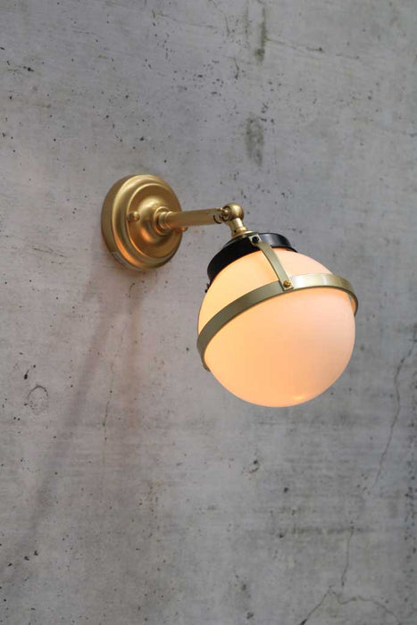 Huxley wall light with long gold arm and small opal shade in tilted position