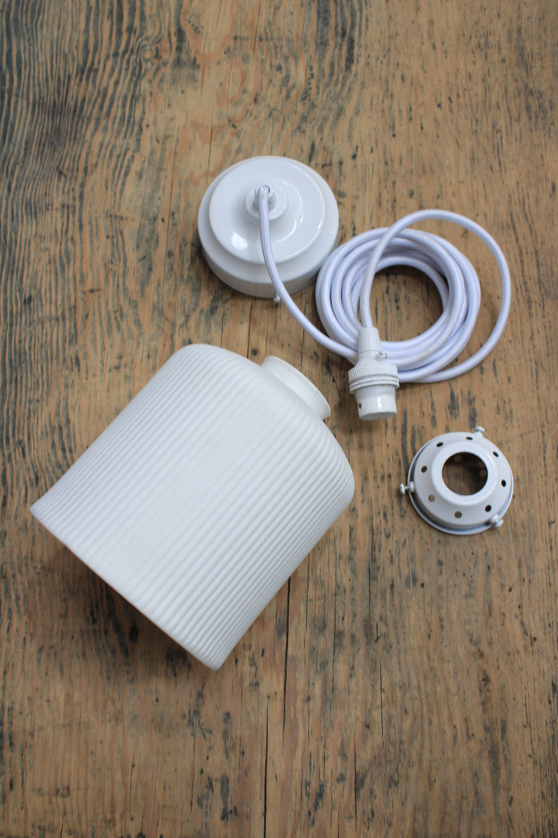 White ceramic shade with white pendant cord and lampholder on a trunkk shot