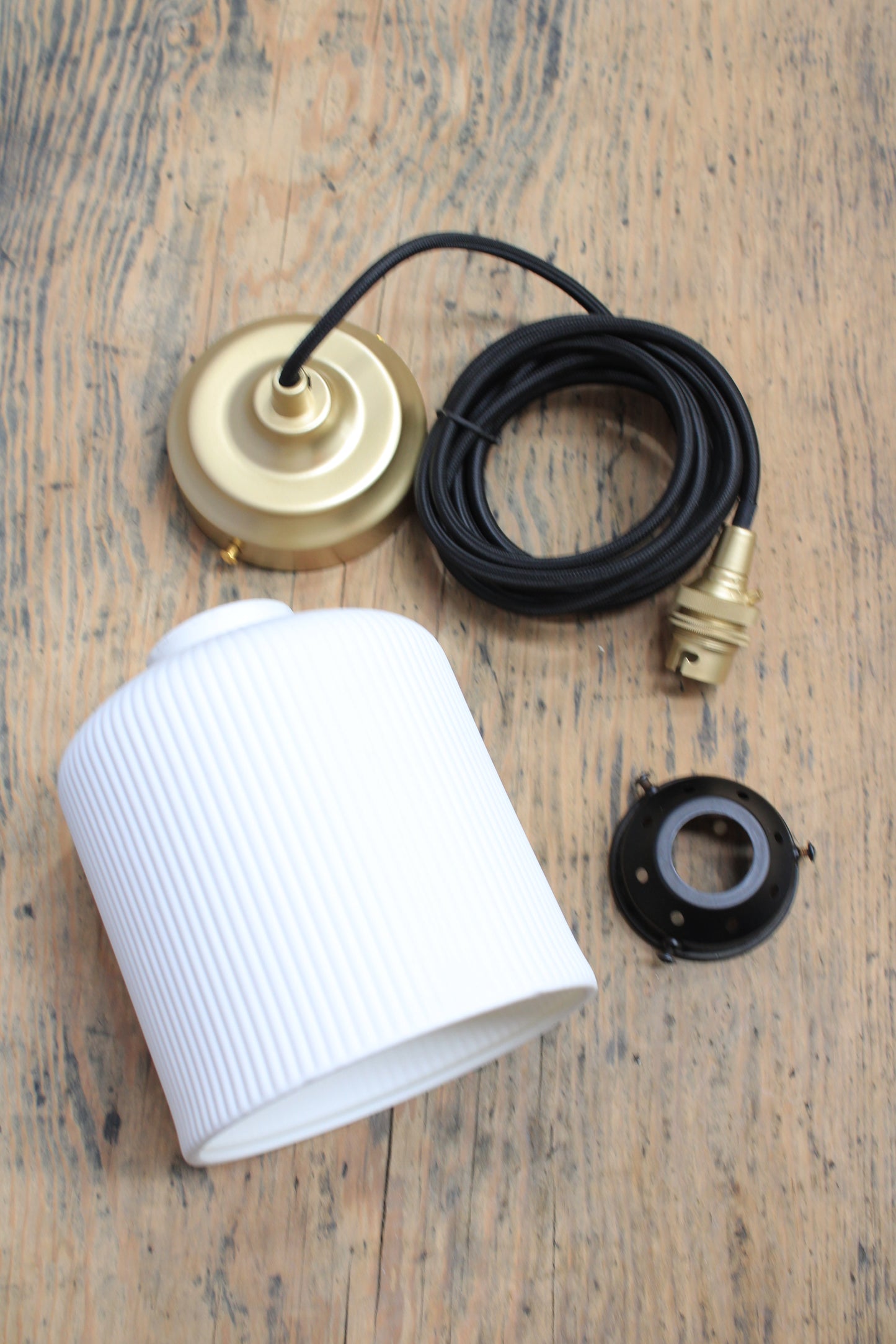 white ceramic shade, brass fitting, black pendant cord, and metal gallery on a trunk shhot